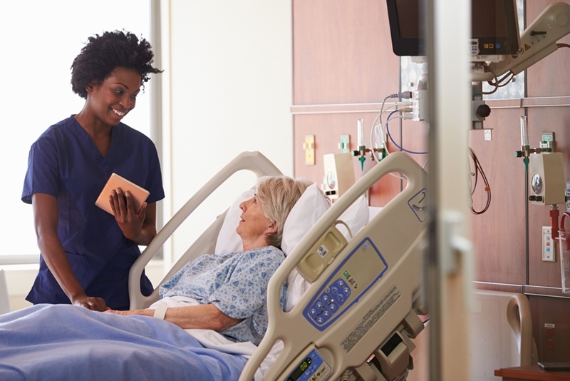 Nurse standing above bed of elderly patient in the hospital. 