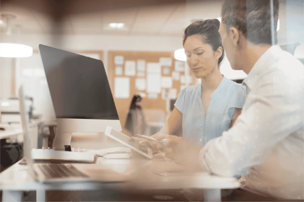 Healthcare administrator and clinical colleague reviewing surgery center scheduling software on a laptop.